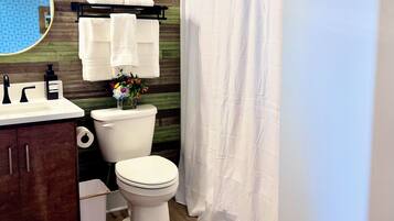 A bathroom with a wooden wall, a toilet, a sink, a mirror, and a shower curtain.