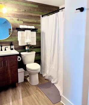 Un baño con pared de madera, inodoro, lavamanos, espejo y cortina de ducha.