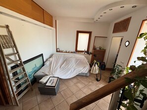 A bedroom with a bed covered in white, a TV on a stand, a ladder, a small table with a picture frame, and a window with blinds. - Fabulous 2-bedroom apartment in Pozzuoli just 2 minutes away from the waterfront (Pozzuoli)