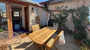 En terrasse med et træbord og stole, en fletstol, krukkeplanter og en stenvæg.