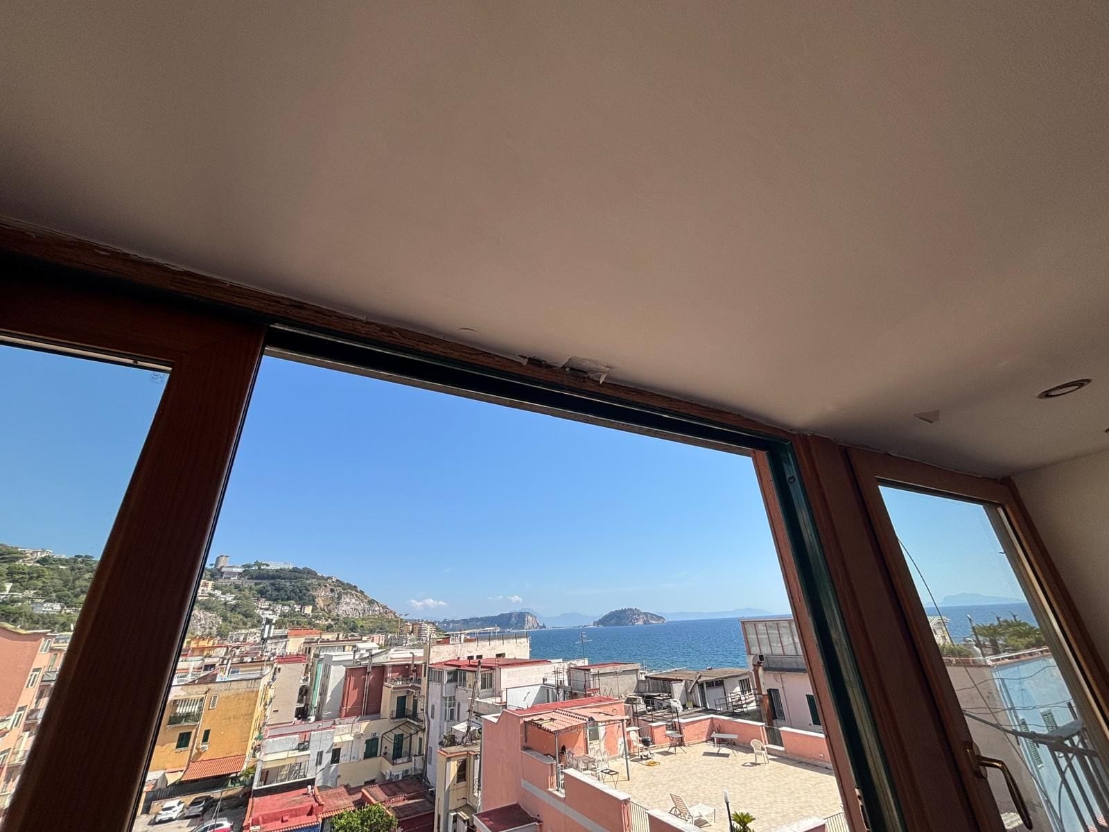 A room with a large window overlooking a coastal cityscape with buildings and a view of the sea.