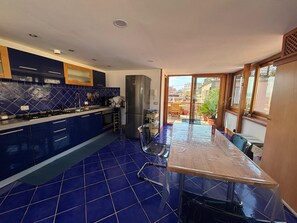 Une cuisine avec des carreaux bleus, un réfrigérateur en acier inoxydable et un coin repas comprenant une table et des chaises.