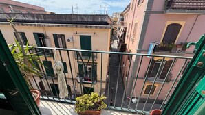 En smal gade i byen med bygninger på hver side, en balkon med en potteplante og en klar himmel.