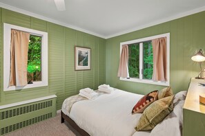 A bedroom with a bed, two windows with curtains, a radiator, a framed picture on the wall, and a bedside lamp. - Private Beach | Game Room | Near Kohler-Andrae (Sheboygan)