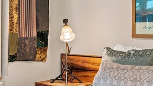 Cama bem arrumada com toalhas brancas dobradas, luminária de cabeceira e cabeceira com almofada florida.