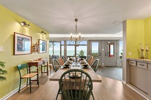 A dining area with a large table, chairs, and a chandelier. There are framed pictures on the walls and a view of the outdoors through the windows. - Private Beach | Game Room | Near Kohler-Andrae (Sheboygan)