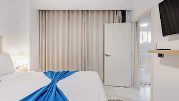 Habitación de hotel con cama, televisión montada en la pared, puerta y ventana con cortinas.