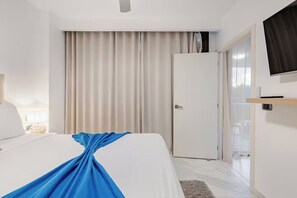 Une chambre d’hôtel avec un lit, un téléviseur fixé au mur, une porte et une fenêtre avec des rideaux.