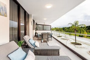 Un balcon aménagé avec un canapé, des chaises et une table, donnant sur un espace paysager agrémenté de palmiers.