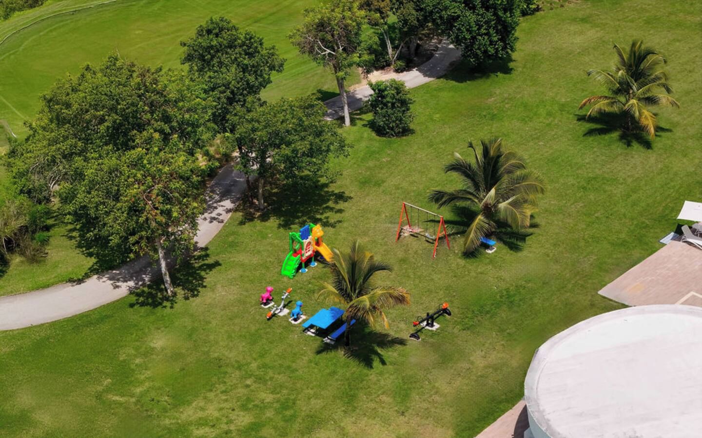 Vue aérienne d’un parc avec des jeux pour enfants, des palmiers et un chemin pavé.