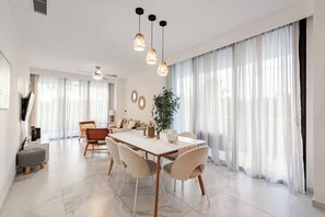 Un espace de salle à manger moderne avec une table blanche, des chaises beige et des luminaires suspendus.