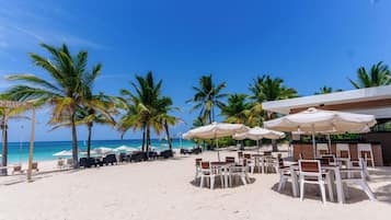 A beachside resort with lounge chairs and umbrellas, palm trees, and a clear blue sky.