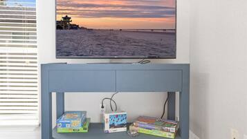 A wall-mounted TV displaying a beach sunset, a blue console table with board games, and a power outlet.