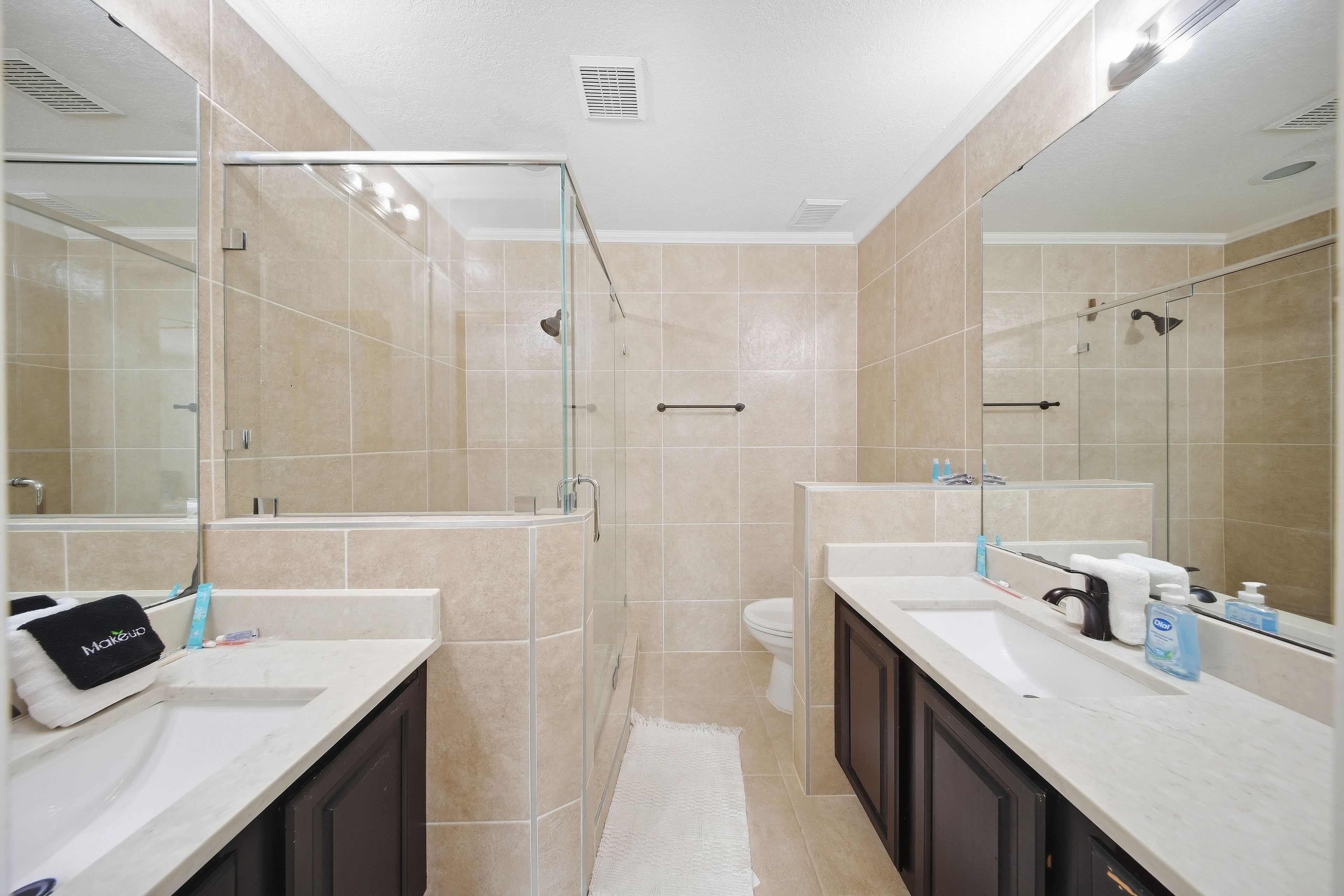 A modern bathroom with two sinks, a glass shower enclosure, and a toilet.