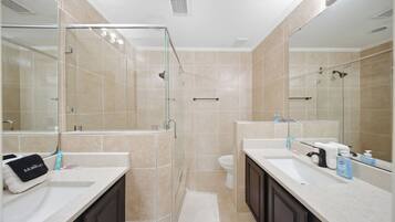 A modern bathroom with two sinks, a glass shower enclosure, and a toilet.