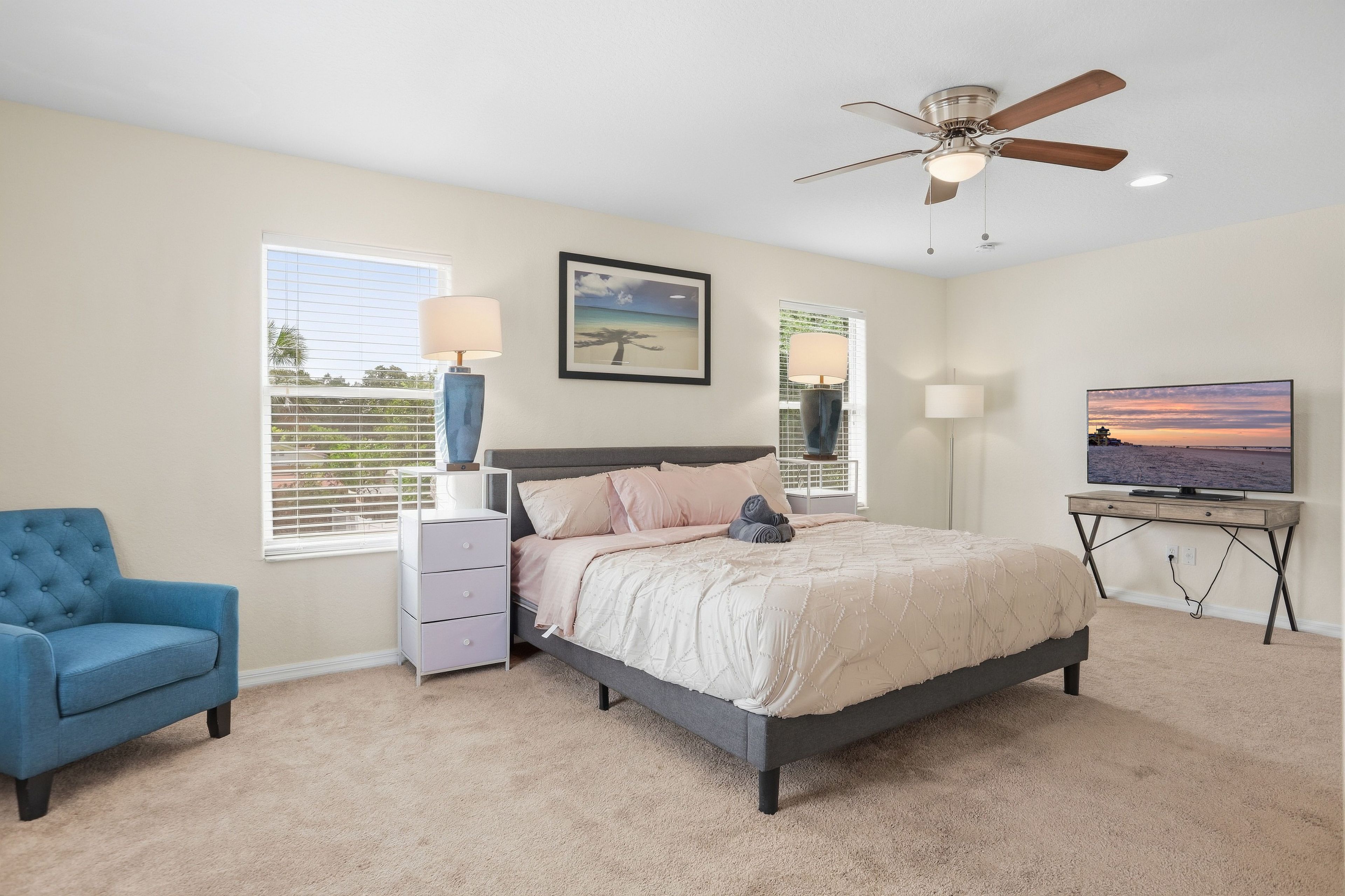 A bedroom with a bed, a chair, a desk, a television, and a ceiling fan.