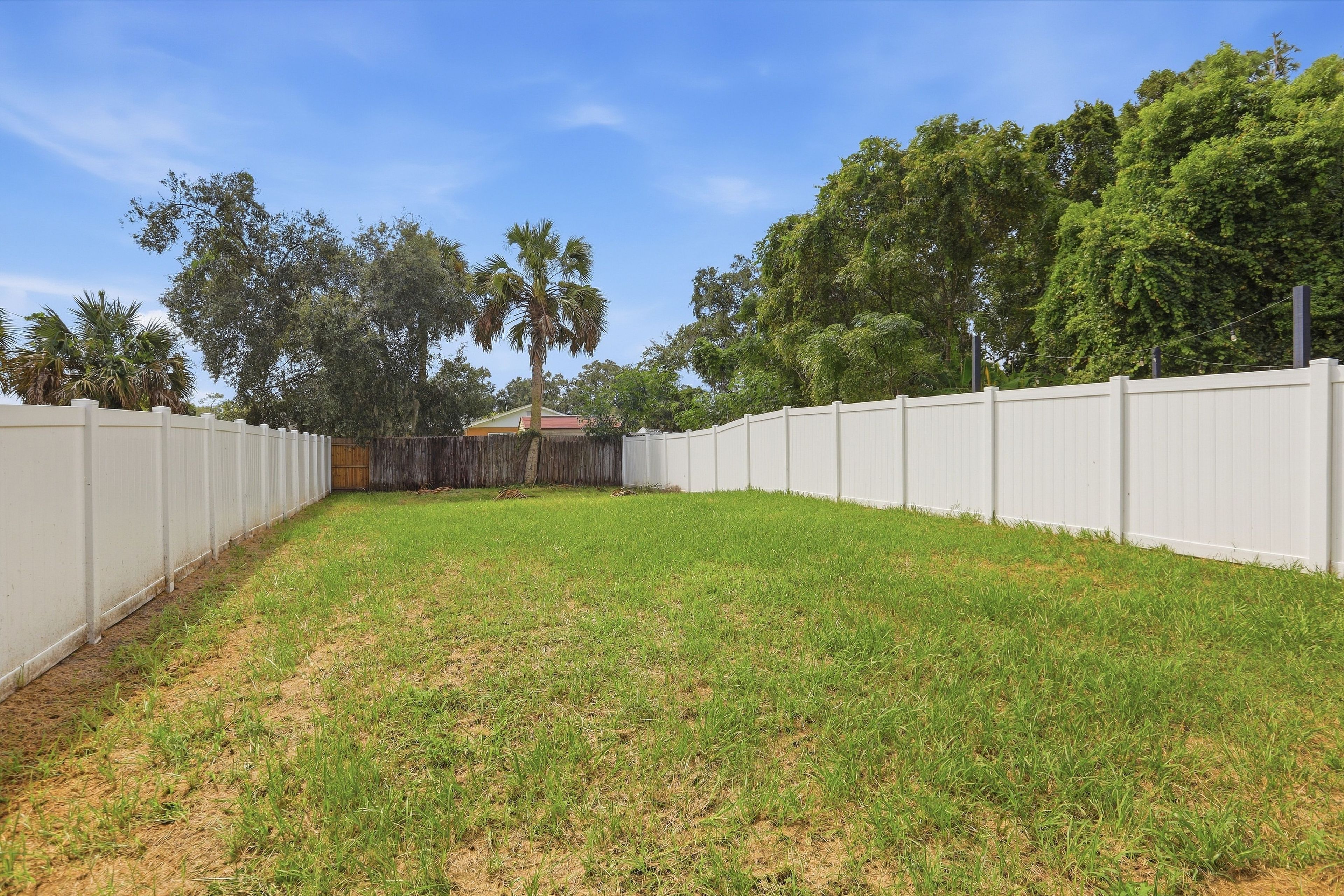 A fenced backyard with a grassy area and trees.