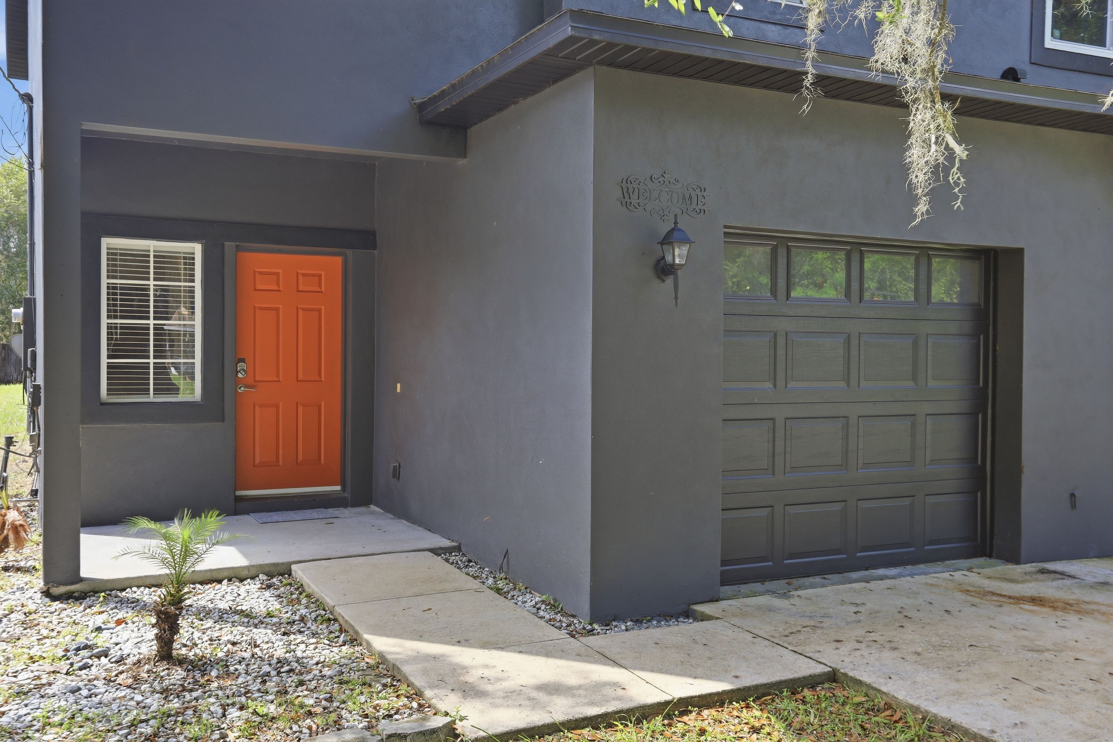 A modern two-story house with a red door, a garage, and a small garden area.