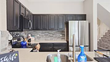 A modern kitchen with dark cabinets, a stainless steel refrigerator, and a countertop with a sink and various kitchen items.