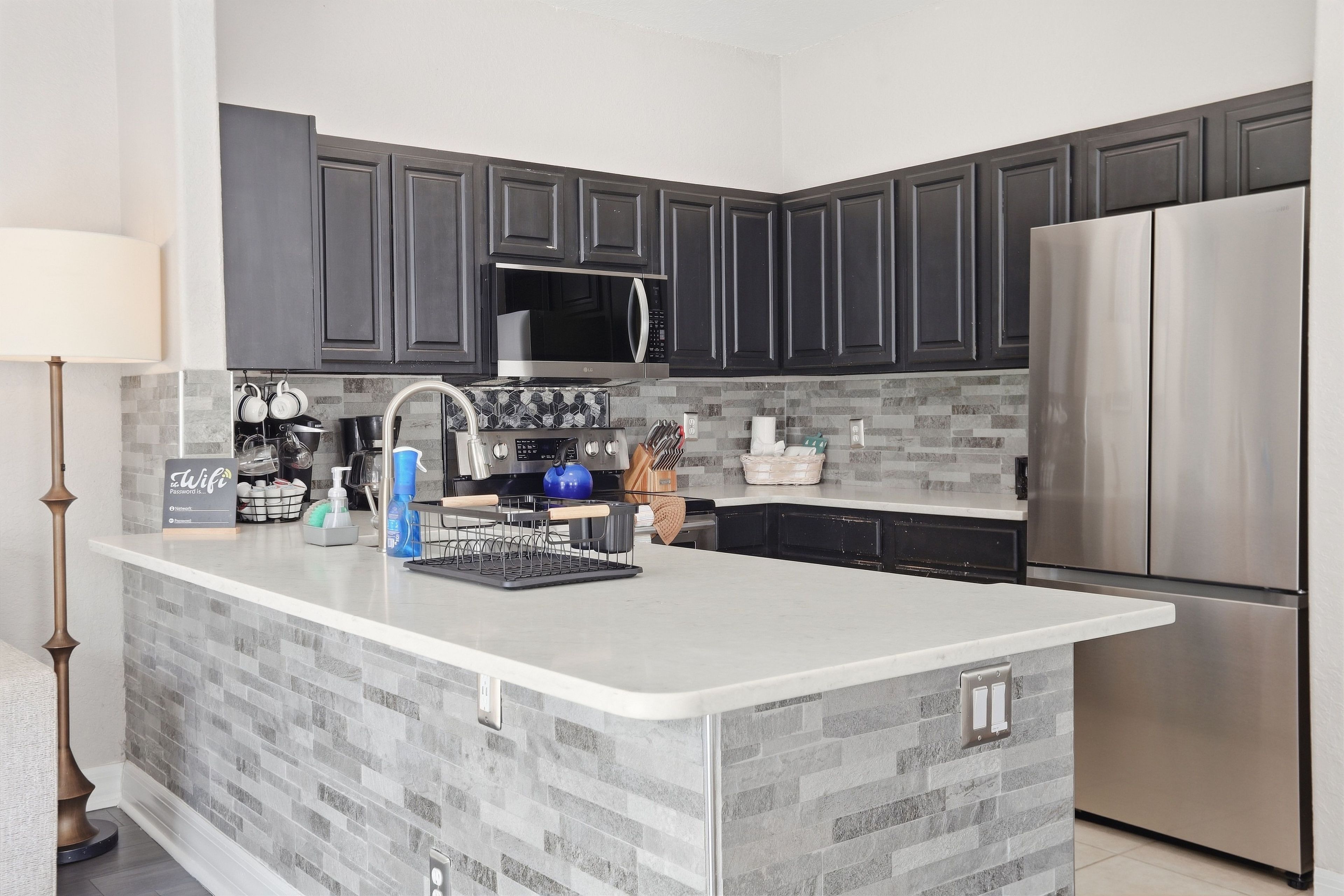 A modern kitchen with dark cabinets, a stainless steel refrigerator, and a built-in microwave.