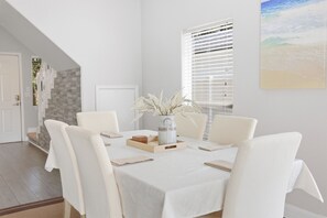 Un coin repas avec une table blanche, des chaises et un vase contenant des fleurs séchées.