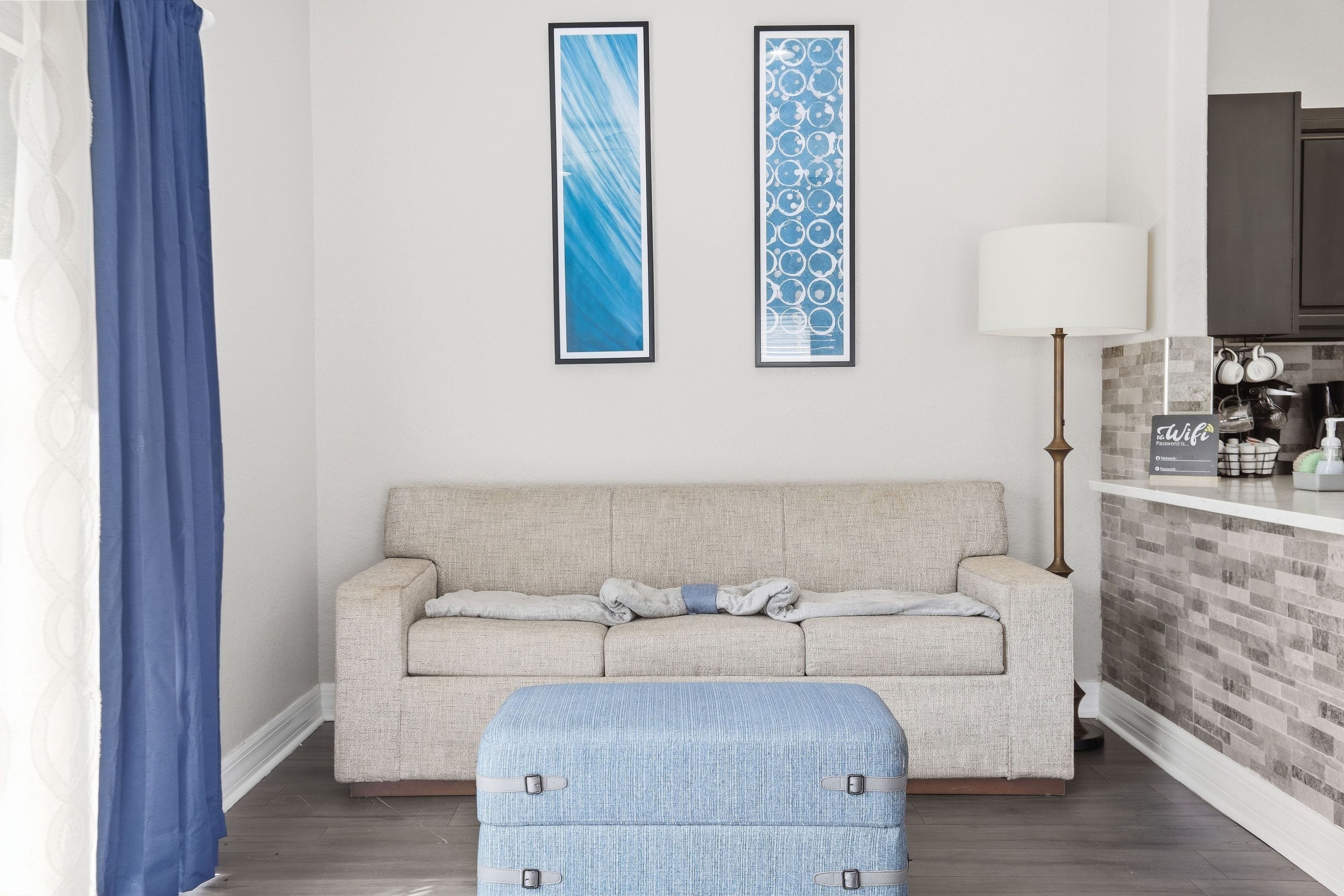 Un salón con un sofá, un reposapiés azul y dos cuadros abstractos enmarcados en la pared.