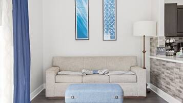 Un salón con un sofá, un reposapiés azul y dos cuadros abstractos enmarcados en la pared.