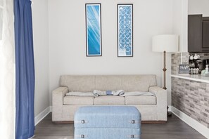 A living room with a sofa, a blue ottoman, and two framed abstract paintings on the wall.