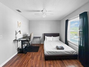 A bedroom with a bed, a desk with a chair, a ceiling fan, and a window with curtains. - Clearwater Comfort 2BR Townhome Near HCA (Clearwater)