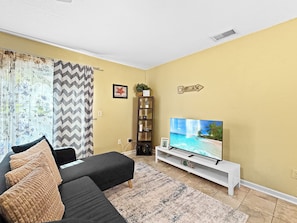 A living room with a black sofa, a television, a patterned rug, and a bookshelf. - Clearwater Comfort 2BR Townhome Near HCA (Clearwater)