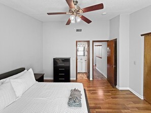 Ein Schlafzimmer mit Bett, Deckenventilator, Kleiderschrank und einem zur Toilette führenden Gang.