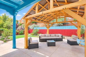 An outdoor patio with a covered seating area, including a sofa and chairs, under a wooden pergola. - Sweeping Views, Arcade, Putting, Chef's Kitchen (Albuquerque)
