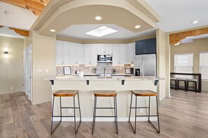 A modern kitchen with a central island, white cabinets, and a microwave. - Sweeping Views, Arcade, Putting, Chef's Kitchen (Albuquerque)