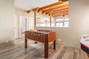 A room with a wooden foosball table, wooden beams on the ceiling, and a window providing natural light. - Sweeping Views, Arcade, Putting, Chef's Kitchen (Albuquerque)