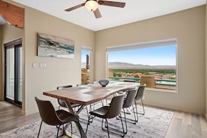 A dining area with a table and chairs, a ceiling fan, and a large window with a view of a landscape. - Sweeping Views, Arcade, Putting, Chef's Kitchen (Albuquerque)