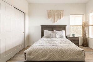 A bedroom with a bed, a nightstand, a window with blinds, and a macrame wall hanging. - Sweeping Views, Arcade, Putting, Chef's Kitchen (Albuquerque)