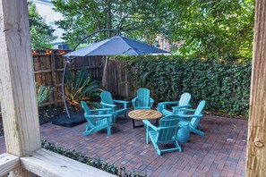 Une terrasse extérieure avec une table en bois et quatre chaises, un parasol noir et une clôture en bois.