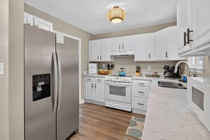 A modern kitchen with white cabinetry, a stainless steel refrigerator, a built-in oven, and a coffee maker. - Savannah Reserve Savannah Breeze Suite & Hot Tub (Savannah)