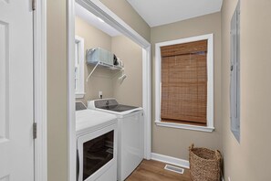 A laundry room with a washing machine, dryer, and a window with blinds. - Savannah Reserve Savannah Breeze Suite & Hot Tub (Savannah)