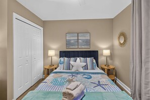 Une chambre à coucher avec un lit, deux lampes de chevet, une décoration en forme d’étoile de mer et un tableau représentant un paysage marin accroché au mur.
