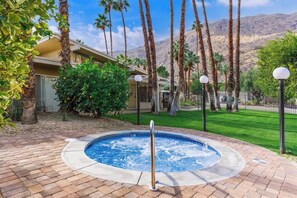 A hot tub surrounded by a brick patio, palm trees, and a building with a mountain backdrop. - Downtown Mid-Century Gem with Pool & Mountain Views, Heated Spa, Sleeps 4! (Palm Springs)
