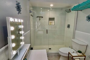 Een badkamer met een wastafel, een spiegel met verlichting, een douche en een toilet.