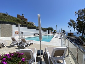 Ein Poolbereich mit Liegestühlen, einem Rettungsbojen und Blick aufs Meer.