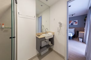 A modern bathroom with a glass shower enclosure, a sink with a towel, and a hairdryer mounted on the wall. - Atmosfera by Bhomy  (São Paulo)