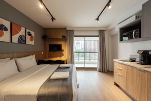 A modern hotel room with a large bed, a desk, a kitchenette, and a view of the city through the window. - Atmosfera by Bhomy  (São Paulo)
