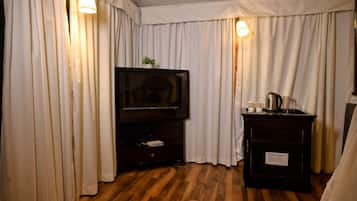 Ein Zimmer mit Fernseher am Flachbildschirm auf einer Holzkommode, weißen Vorhängen und einem kleinen Tisch mit Wasserkocher und Tassen.