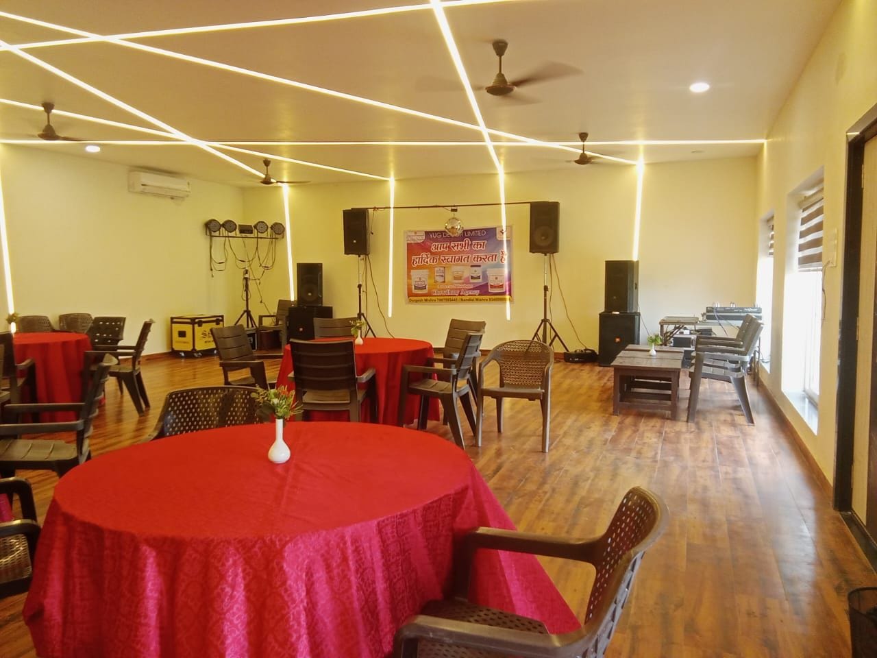 Un salón de conferencias con varias mesas, sillas, ventiladores de techo y altavoces.