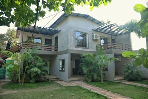 A two-story building with a flat roof, multiple windows, and a balcony. There are potted plants and a paved pathway leading to the entrance. - KINGFISHER RESORT (Mocha)