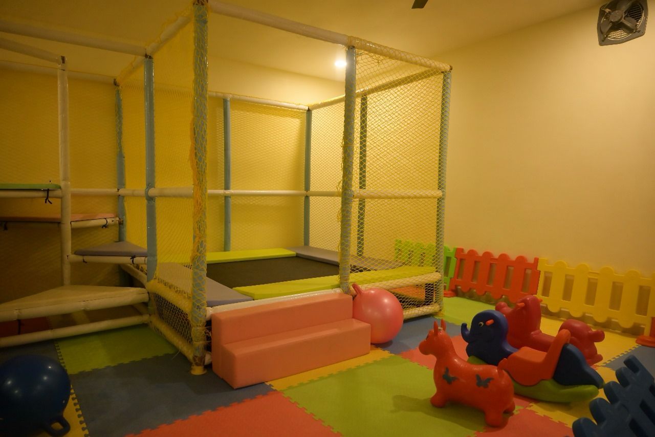 A play area with a trampoline, soft play steps, and colorful play structures.