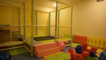 A play area with a trampoline, soft play steps, and colorful play structures.